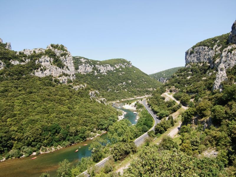 Vue panoramique d'une rivière sinueuse dans une vallée rocheuse et boisée sous un ciel bleu lumineux.