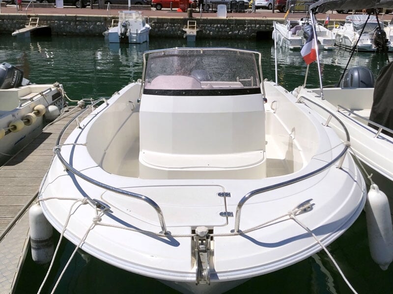 Un bateau de plaisance blanc amarré à un quai avec d'autres bateaux, dans un port calme