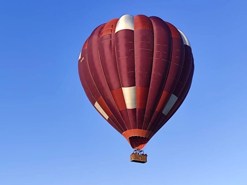Montgolfière rouge et blanche flottant dans un ciel bleu clair sans nuages, vue de dessous.