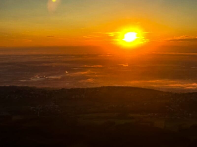 Coucher de soleil brillant au-dessus d'un paysage vallonné avec des nuages bas et une lumière dorée.