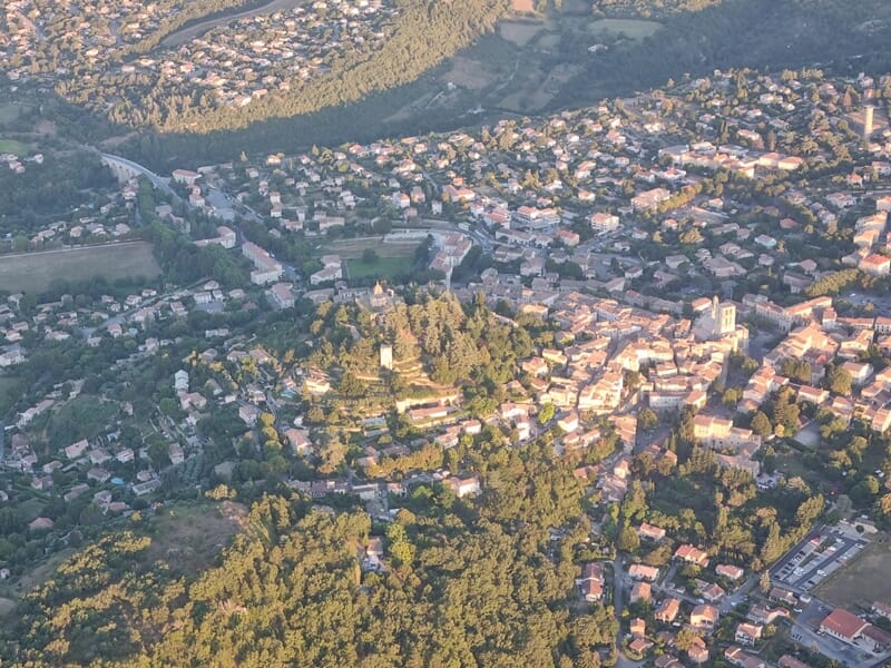 Vue aérienne d'une ville entourée de collines et de forêts prise depuis une montgolfière.