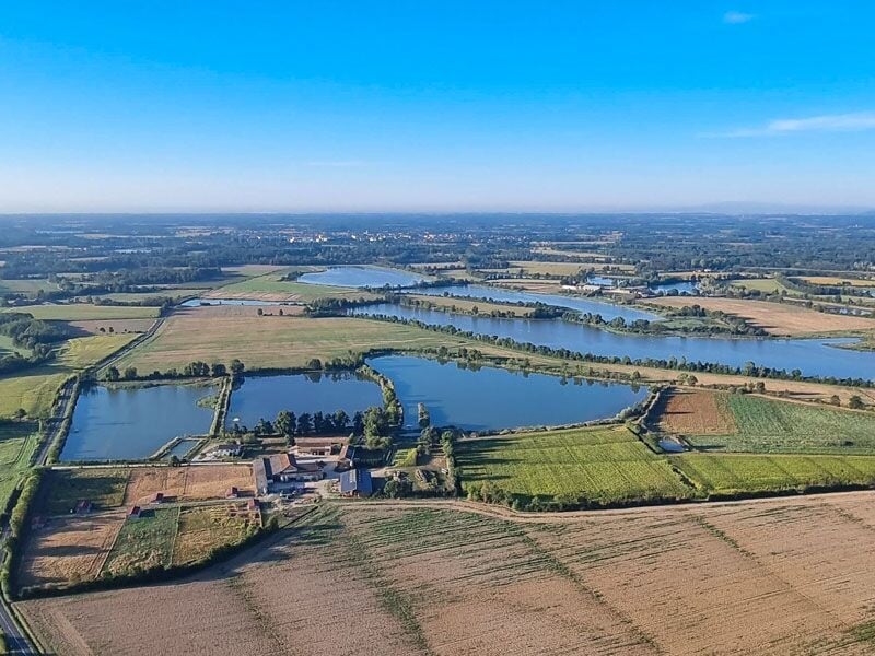 Paysage rural vu du ciel avec plusieurs plans d'eau, champs cultivés et zones boisées sous un ciel bleu.