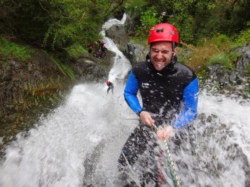 Homme en casque rouge descend en rappel dans une cascade lors d'une activité de canyoning en pleine nature.