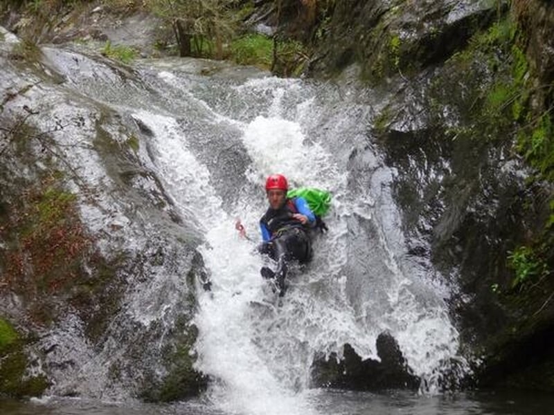 Personne glissant sur un toboggan naturel d'eau vive en canyoning, entourée de rochers et végétation.
