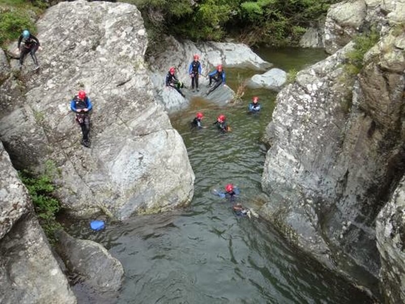 Groupe de personnes en combinaisons et casques se baignant dans une rivière encaissée entre des rochers.
