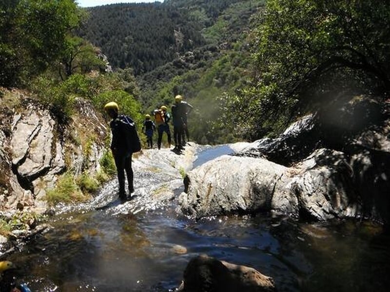 Personnes en tenue de canyoning marchant sur un rocher plat au bord d'une rivière en milieu naturel.