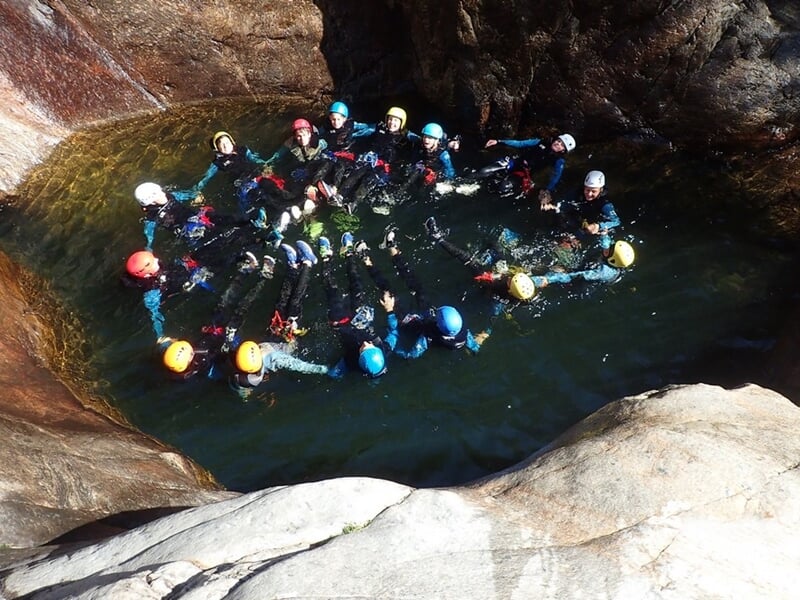 Groupe de canyoning formant un cercle dans une piscine naturelle d'eau claire entourée de rochers.