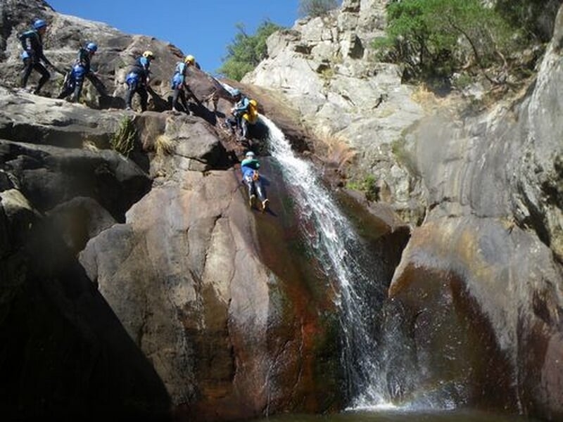 Participants au canyoning escaladant une cascade rocheuse avec équipement de sécurité et casques.