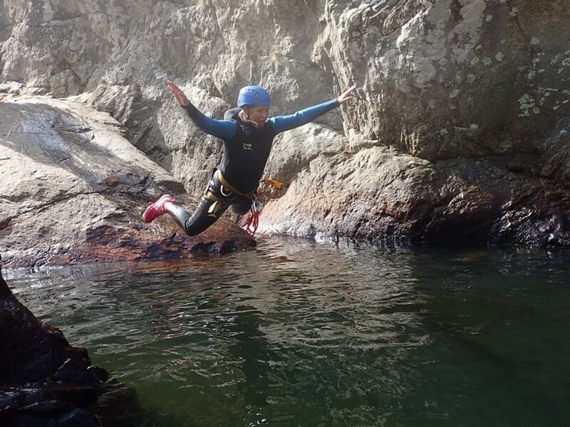 Enfant en combinaison de plongée sautant dans une eau calme depuis un rocher lors d'une sortie canyoning.