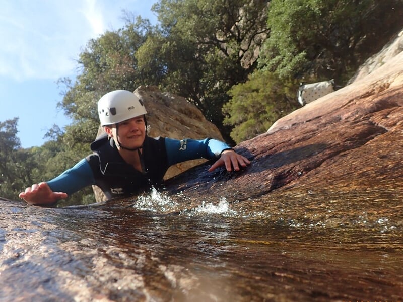 Personne en casque blanc glissant sur une surface rocheuse mouillée dans un environnement naturel.