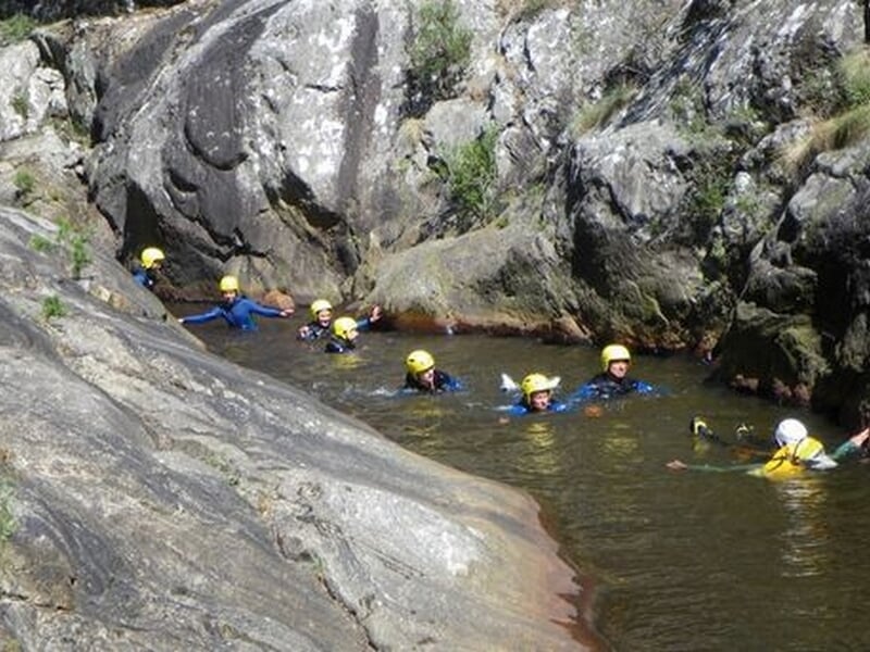 Groupe de personnes en combinaisons et casques nageant dans une rivière étroite entourée de rochers.
