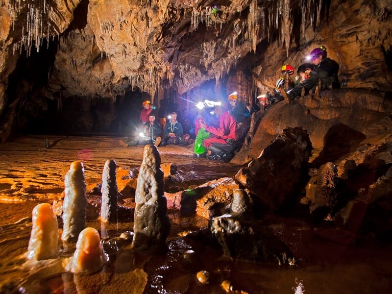 Groupe de spéléologues avec lampes frontales explorant une grande salle souterraine ornée de stalagmites.