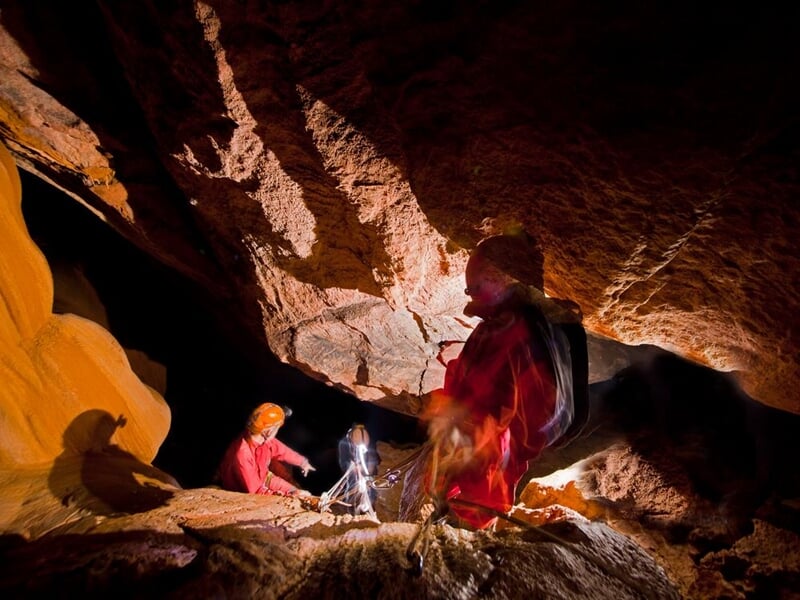Personnes en tenue de spéléologie équipées de casques et lampes explorant une cavité rocheuse.