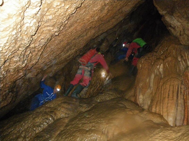 Spéléologues progressant dans une grotte avec formations rocheuses, éclairés par leurs lampes frontales.