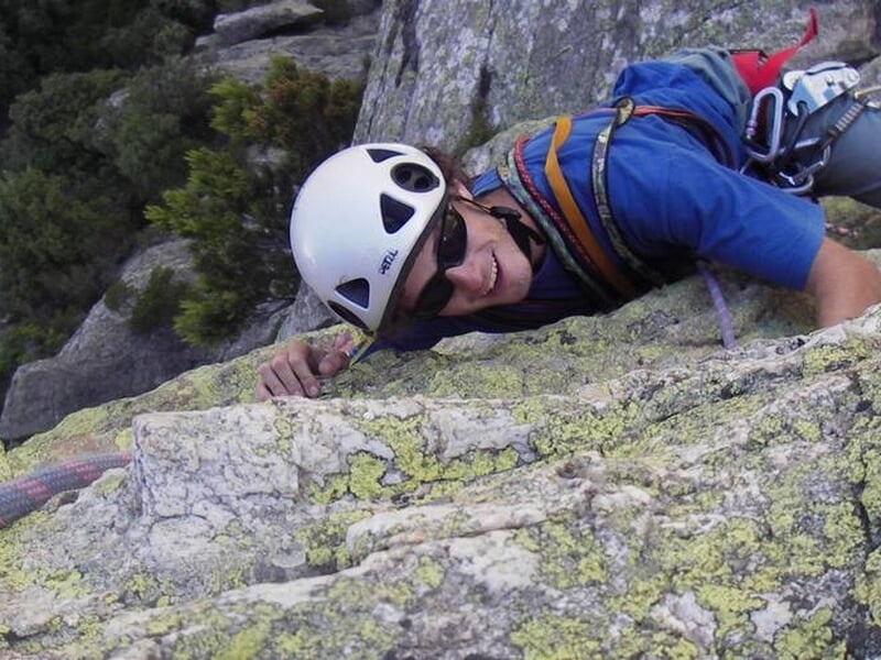 Homme souriant en casque blanc escalade une falaise rocheuse avec équipement de sécurité complet.