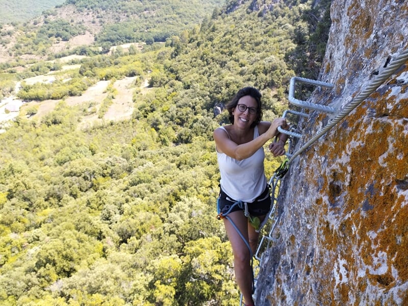Deux personnes en casque et harnais progressent sur une via ferrata accrochée à une falaise rocheuse.