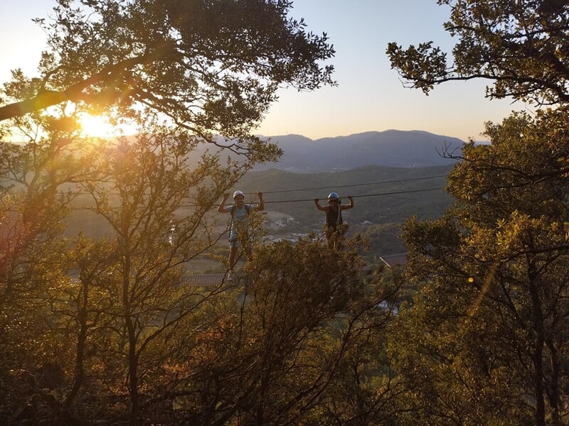 Personne en casque et harnais avance sur une via ferrata rocheuse avec paysage naturel en arrière-plan.
