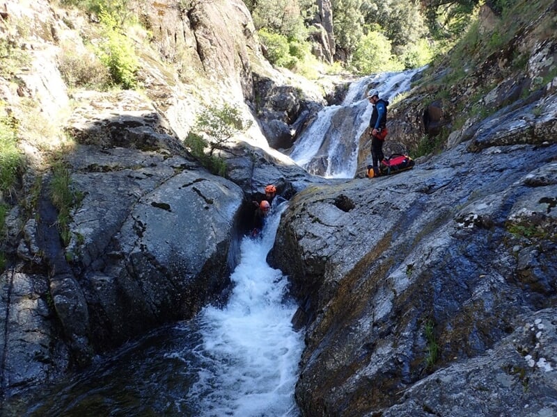 Personne en combinaison rouge descendant une cascade rocheuse en rappel dans un canyon naturel.