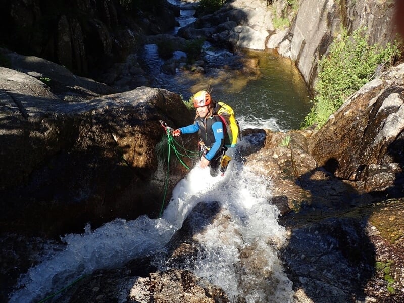 Personne en combinaison bleue descendant une cascade en rappel dans un canyon avec de l'eau vive.