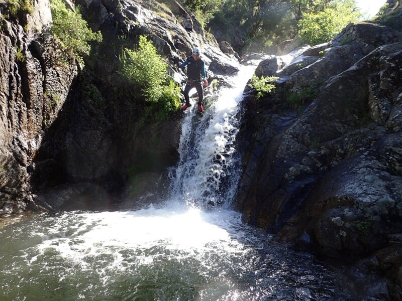 Personne en combinaison rouge escaladant une paroi rocheuse humide dans un canyon.
