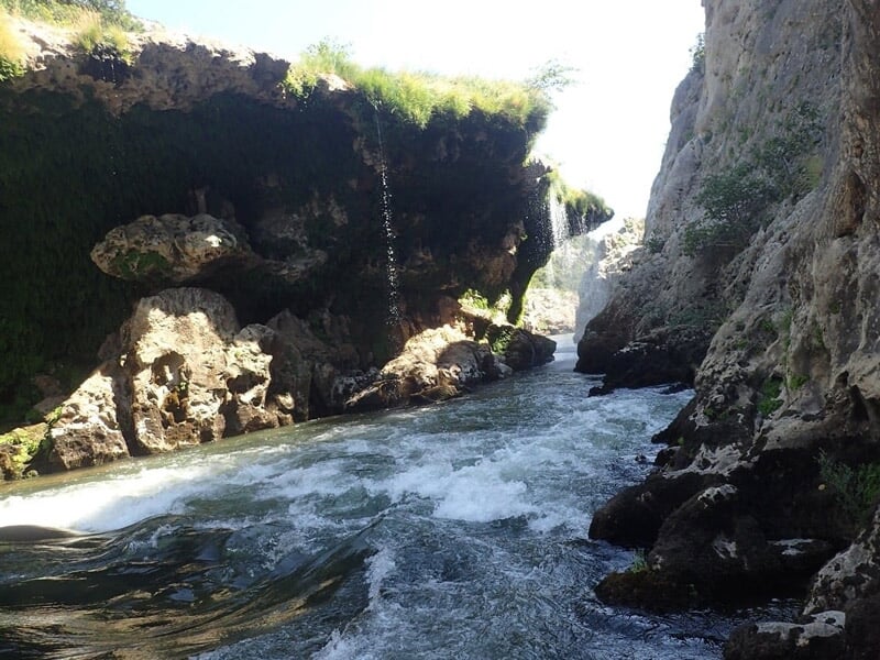 Personne en combinaison rouge sautant dans une eau claire entourée de rochers lors d'une sortie canyoning.
