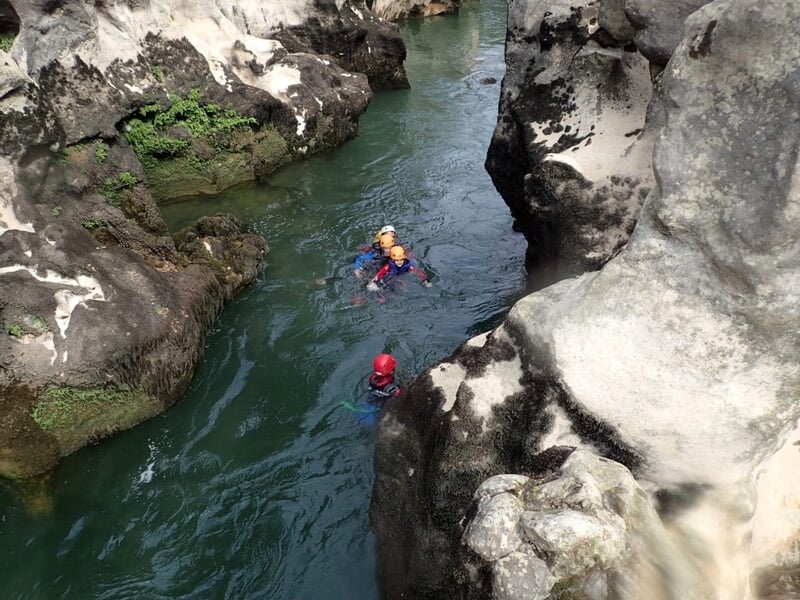 Personne en combinaison rouge descendant en rappel une cascade dans un canyon rocheux et verdoyant.