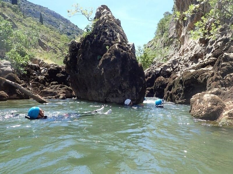 Personne en combinaison rouge marchant près d'une cascade dans un paysage naturel de canyoning.