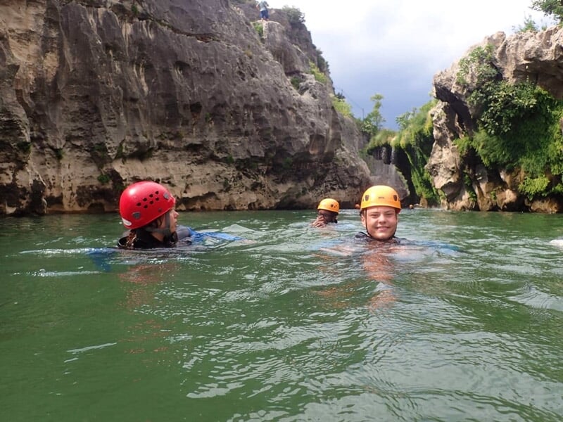Groupe de personnes en combinaison posant souriants devant une cascade dans un canyon rocheux.