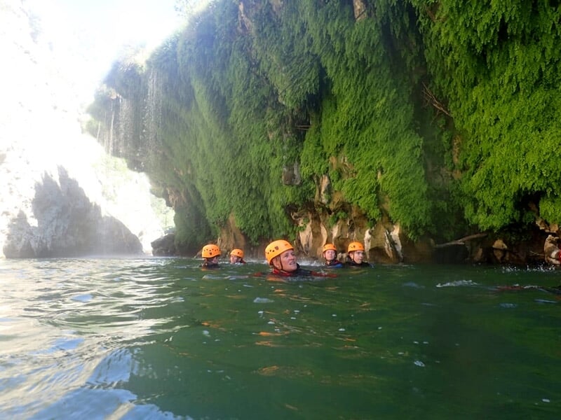 Personne en combinaison bleue descendant une cascade en rappel dans un canyon avec de l'eau vive.