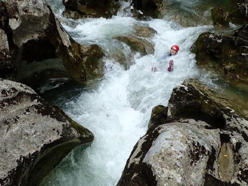 Personne glissant dans un courant d'eau vive entre des rochers lors d'une descente en canyoning.