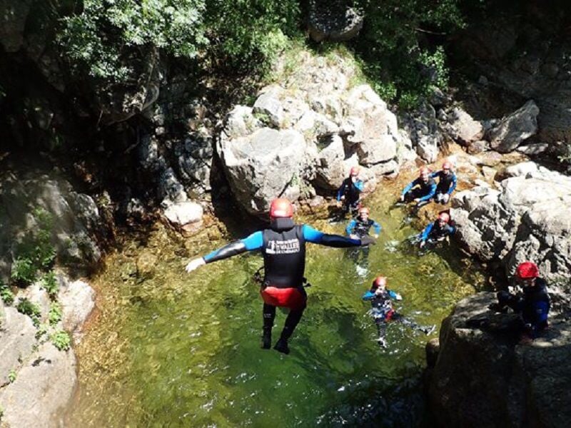 Groupe de personnes en combinaison noire sautant dans une piscine naturelle formée par une cascade.