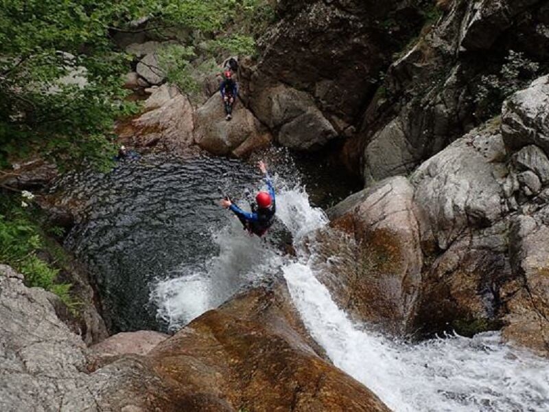 Personne en combinaison rouge sautant dans une eau claire entourée de rochers lors d'une sortie canyoning.
