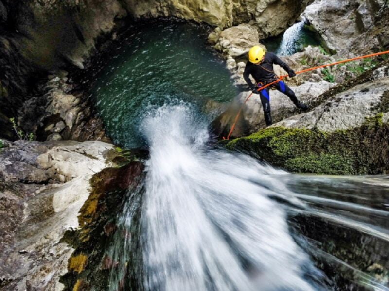 Personne en combinaison bleue sautant dans une rivière encaissée avec des rochers et de la végétation.