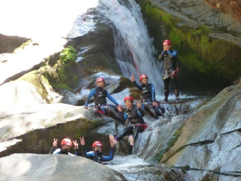 Personne en combinaison rouge marchant près d'une cascade dans un paysage naturel de canyoning.