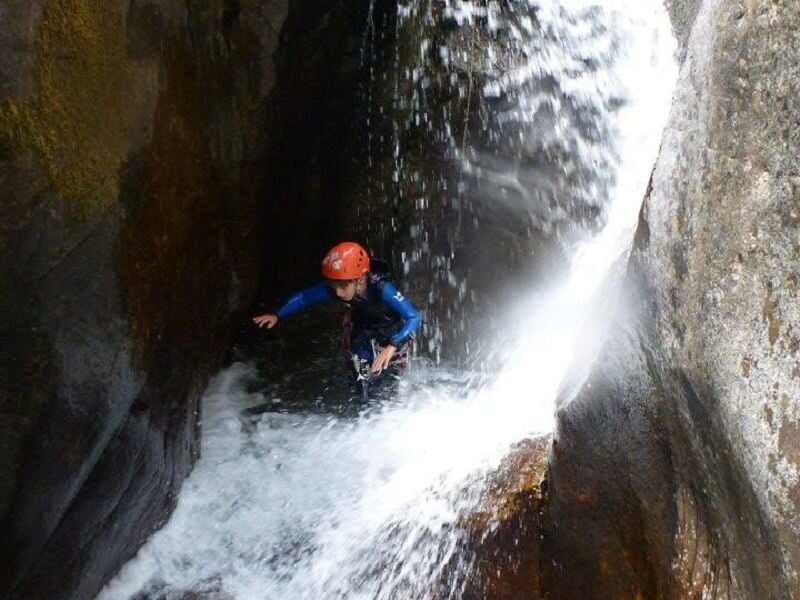 Personne en combinaison bleue descendant une cascade en rappel dans un canyon avec de l'eau vive.