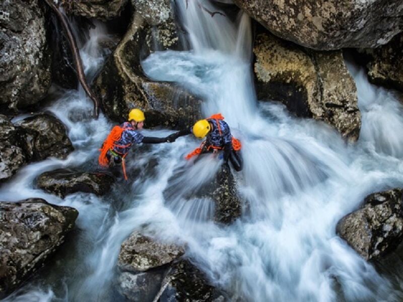 Personne en combinaison rouge escaladant une paroi rocheuse humide dans un canyon.