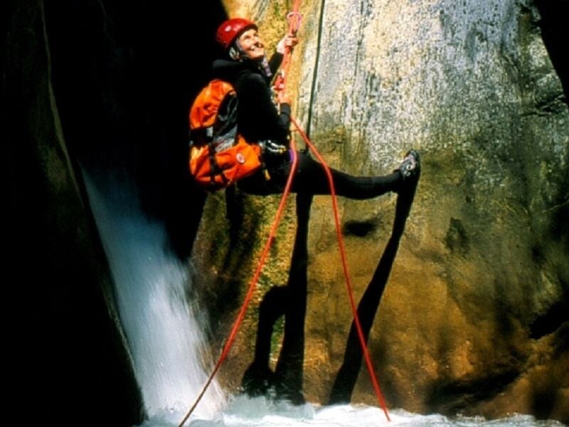 Deux personnes en combinaison et casque rouge aidant à descendre une cascade en canyoning.