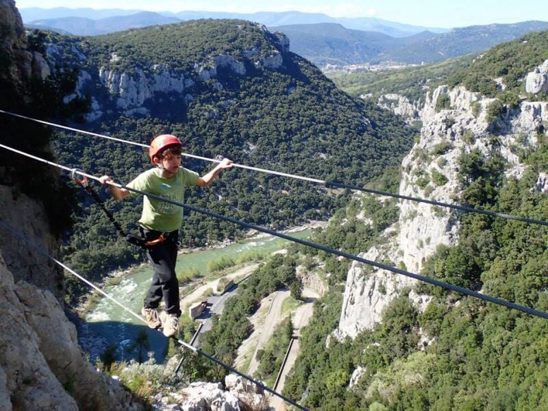 Personne en équipement de via ferrata marchant sur un câble suspendu au-dessus d'une vallée.