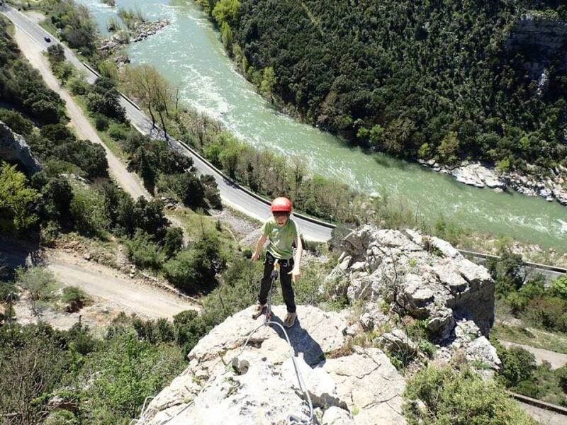 Personne en équipement de via ferrata progressant sur une paroi rocheuse avec un casque rouge.