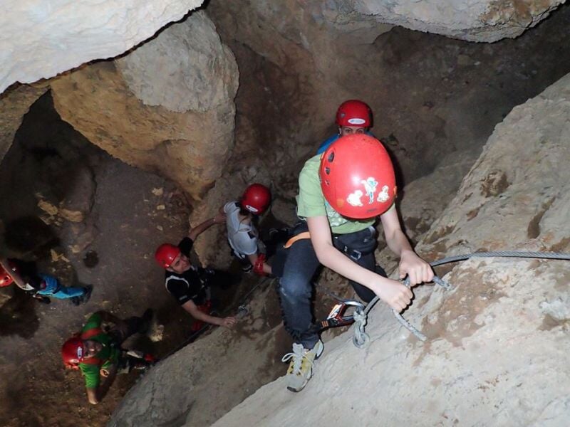 Personne en équipement de via ferrata marchant sur un câble suspendu avec un sac à dos orange.