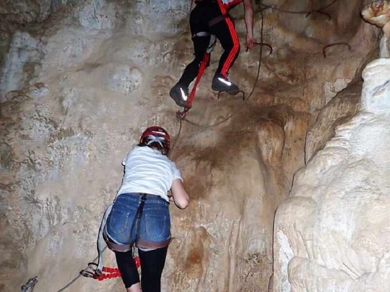 Personne en équipement de via ferrata progressant sur une paroi rocheuse avec un casque rouge.