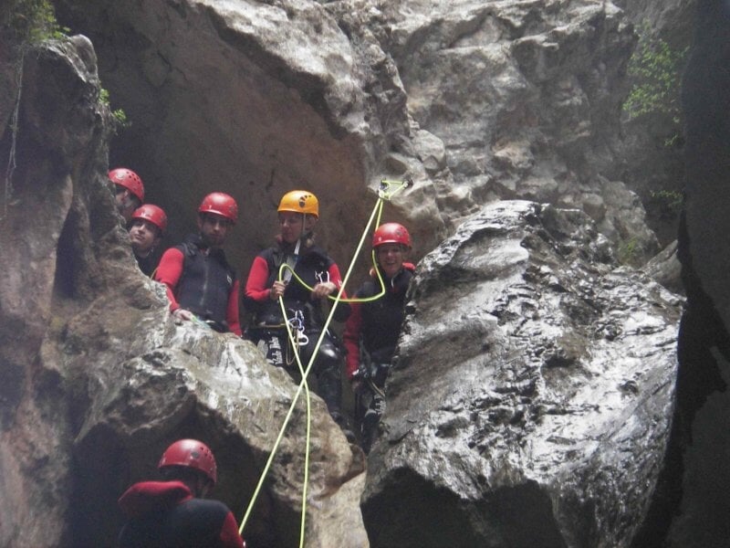 Groupe de personnes en combinaison et casque rouge dans un canyon rocheux, préparant une descente en rappel.