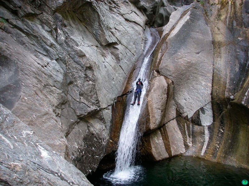 Personne en combinaison descend en rappel une cascade étroite dans un canyon rocheux avec eau en contrebas.