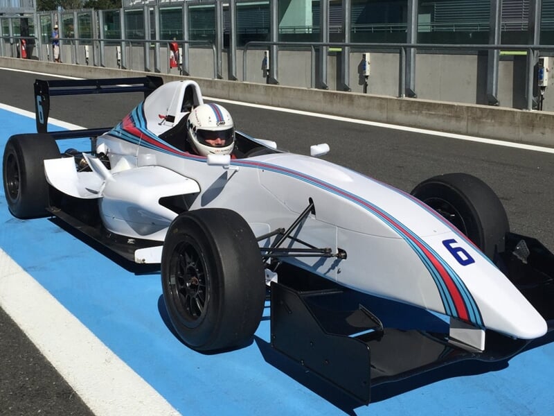 une formule renault arrêtée à un stand avec un pilote dans le cockpit
