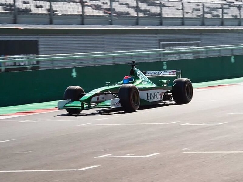 une monoplace de course verte sur un circuit avec un stand en arrière plan