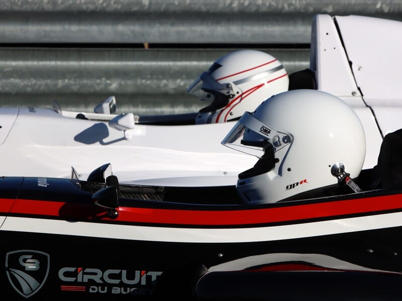 Deux pilotes en casque blanc dans des monoplaces de course sur le circuit de Magny-Cours lors d'un stage de pilotage.