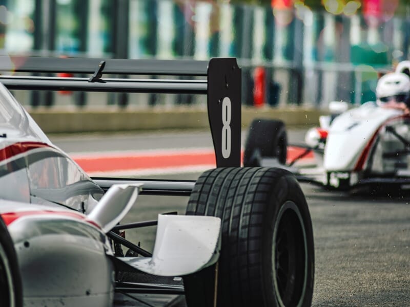 Vue rapprochée de la roue arrière d'une monoplace de course avec une autre voiture en arrière-plan.