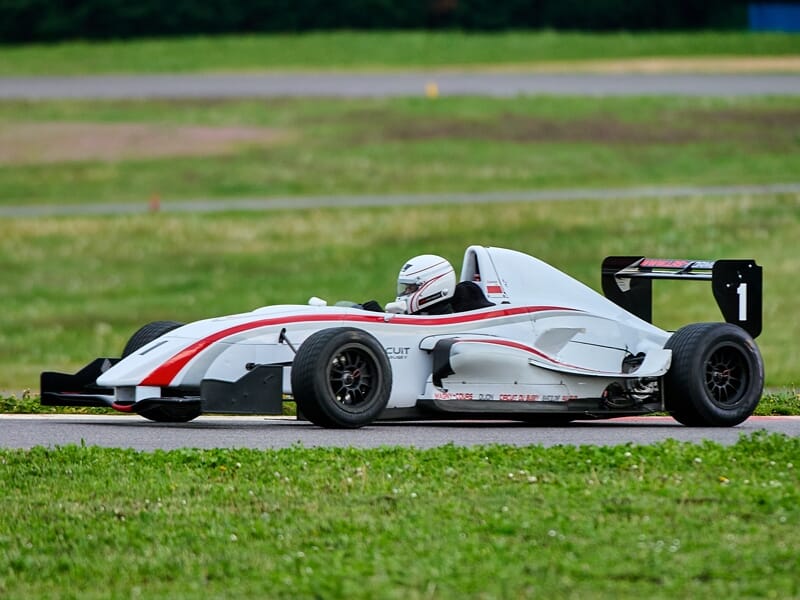 Monoplace blanche et rouge en pleine course sur une piste avec un pilote casqué au volant.