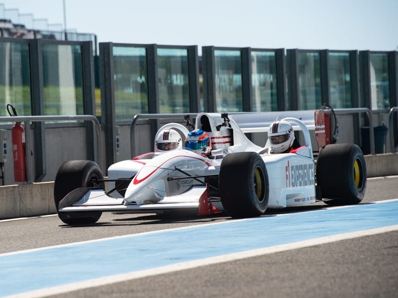 Monoplace de Formule 1 blanche avec deux pilotes casqués roulant sur la piste du circuit de Barcelone-Catalogne.