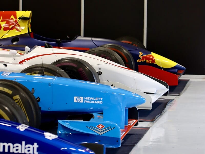 Alignement de plusieurs monoplaces de Formule 1 aux couleurs vives dans un garage, prêtes pour la course.